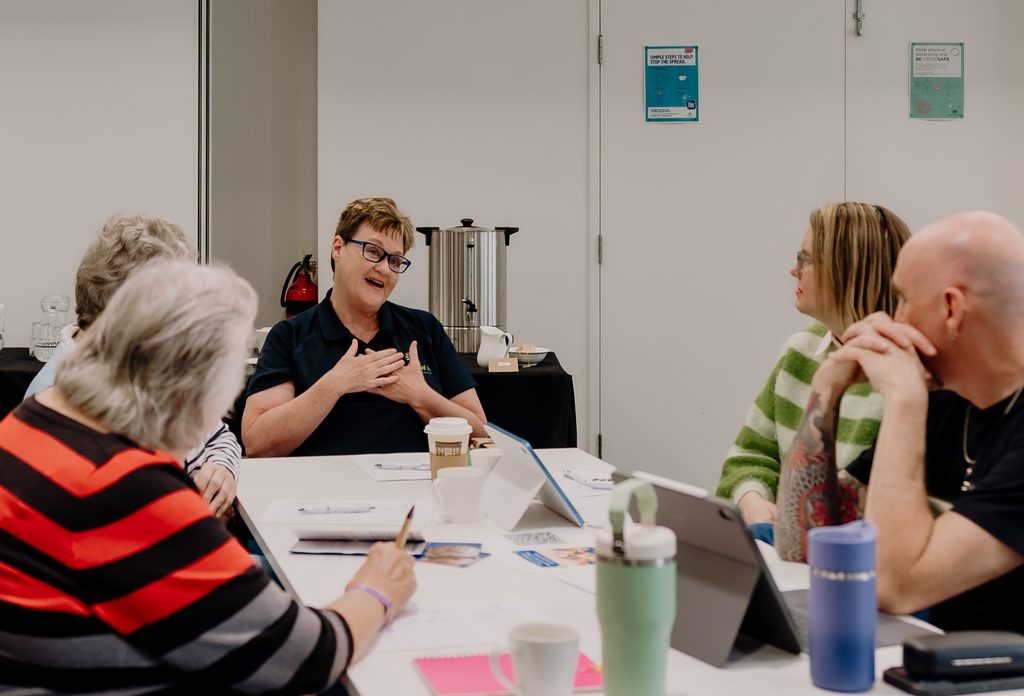 Participants discussing peer support group facilitation during an Alike WA workshop, seated together around a table.